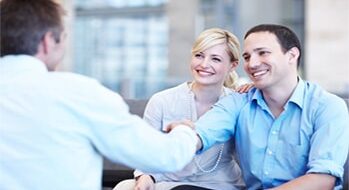 Smiling young couple shaking hands with their property consultant